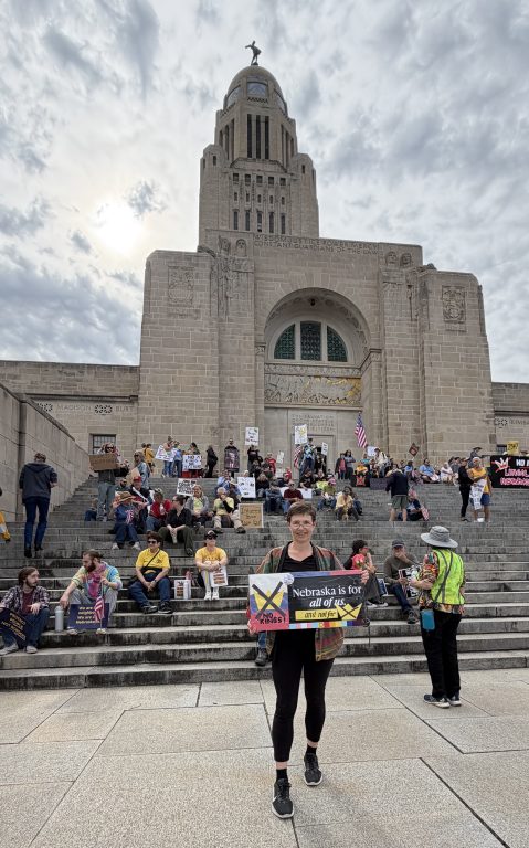 Antje Anderson, No Kings Rally, Lincoln, NE 10-18-2025, with protest sign. Lincoln Capitol in the background.